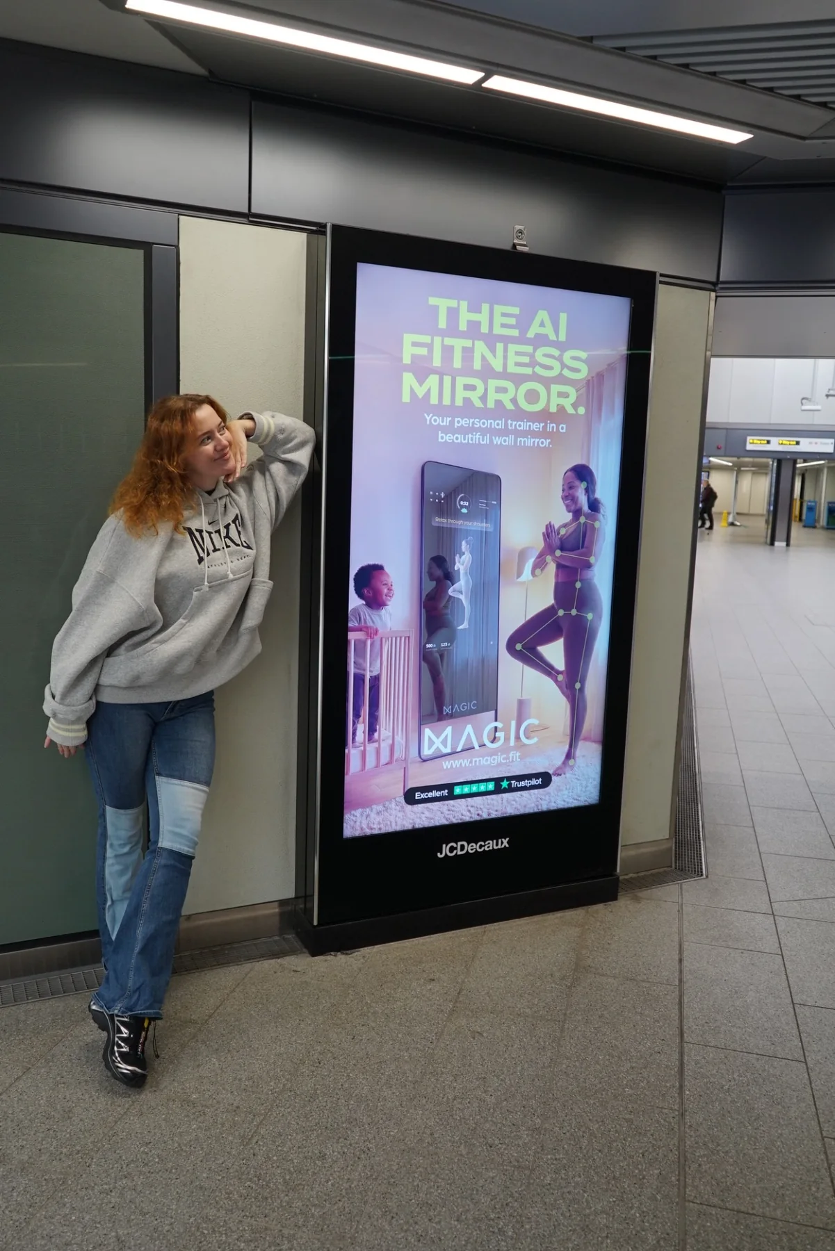 Kate Rubina beside a MAGIC AI campaign display at a major London train station